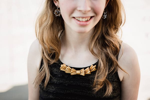 Dívka má na sobě náhrdelník styl mašle a náušnice upcyklované z kapslí